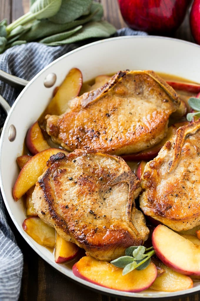 A pan of apple pork chops garnished with fresh sage.