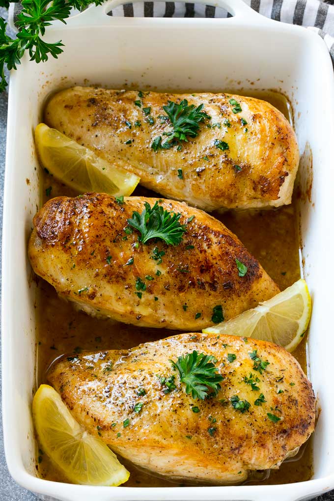 A baking dish full of lemon chicken coated in sauce and garnished with lemons and parsley.