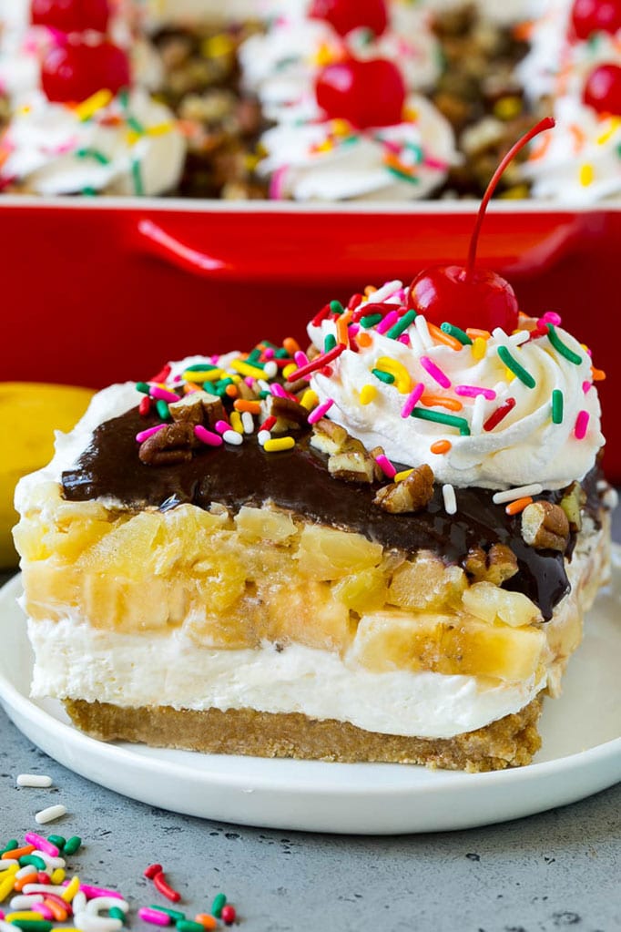 A slice of banana split cake with layers of graham cracker, cheesecake, bananas and pineapple.