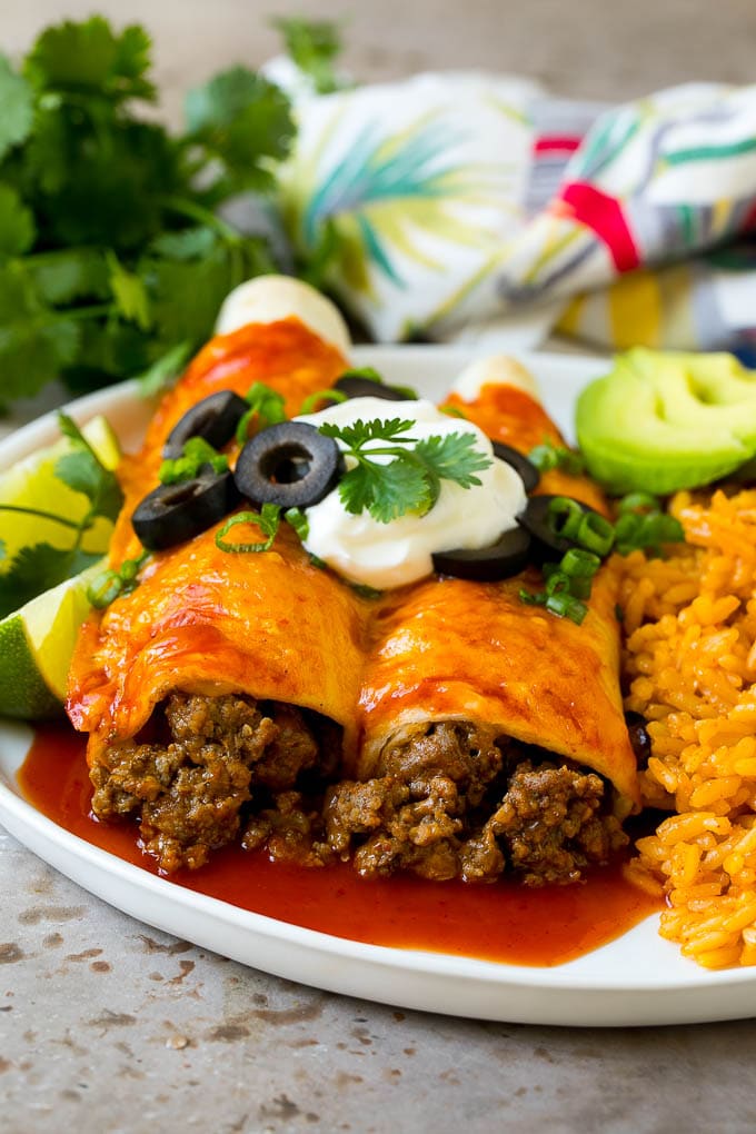 A plate of beef enchiladas topped with sour cream, olives and green onions.