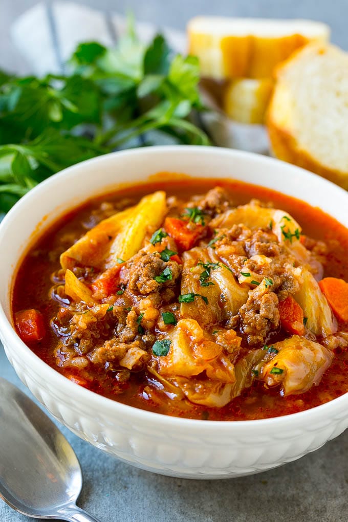 A bowl of unstuffed cabbage soup with bread and parsley.