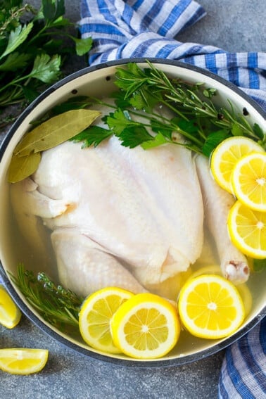 Chicken brine in a pot with a whole chicken, lemons, herbs and spices.