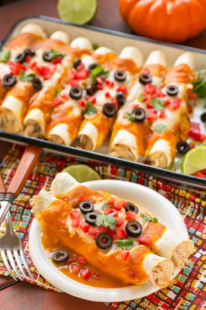 Pumpkin enchiladas on a small plate with a tray of enchiladas behind them.