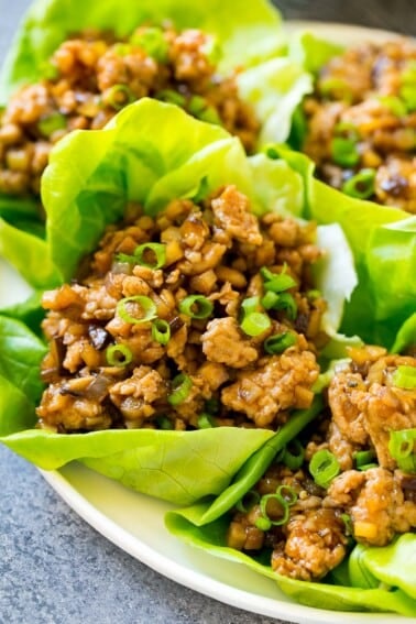 Chicken lettuce wraps on a serving plate, garnished with green onions.