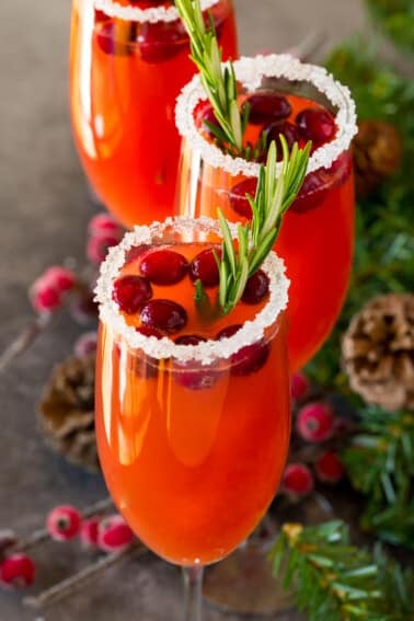 A cranberry mimosa with a sugared glass rim, and a garnish of cranberries and rosemary.