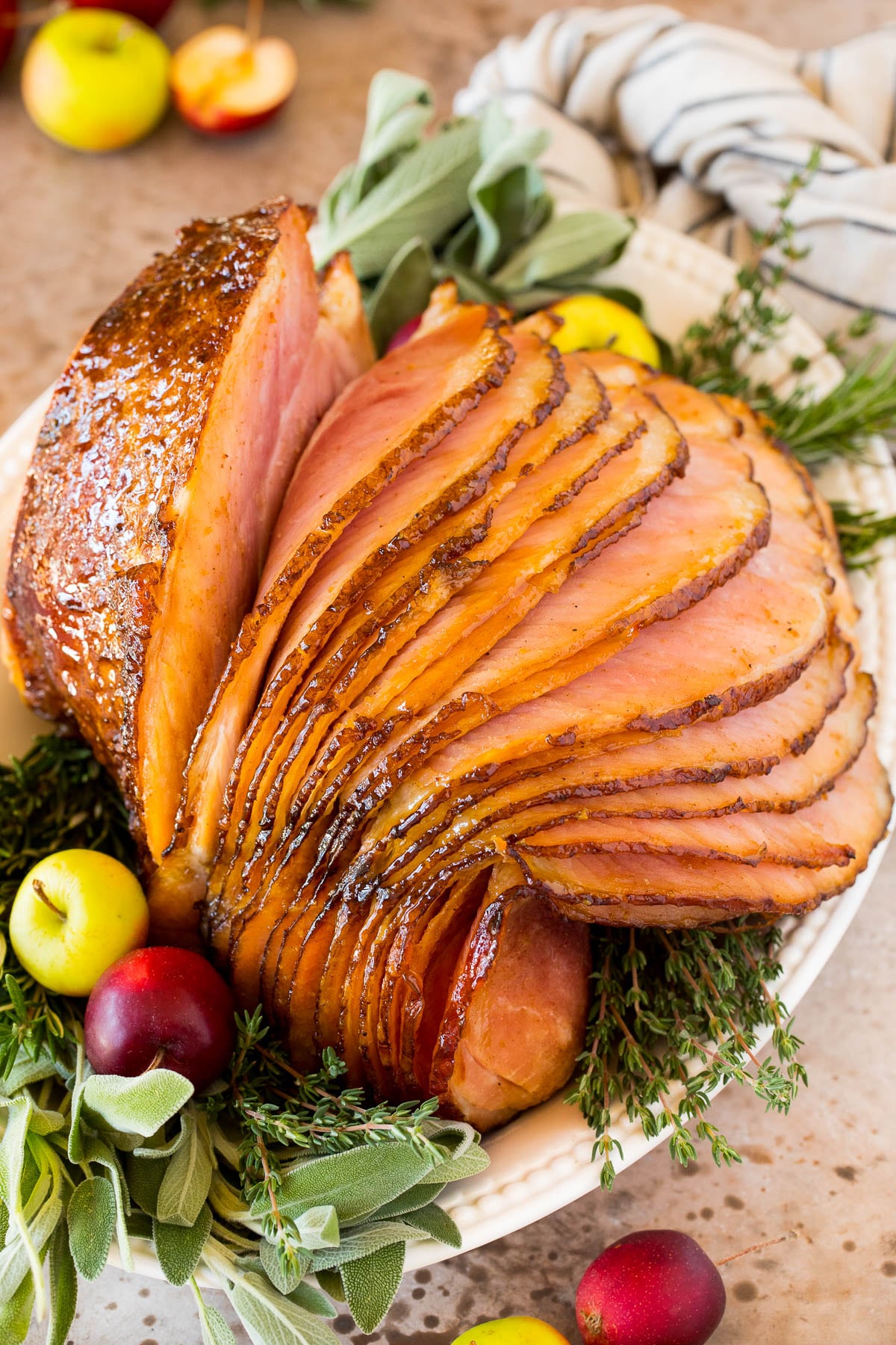 A glazed Easter ham on a platter garnished with herbs and apples.