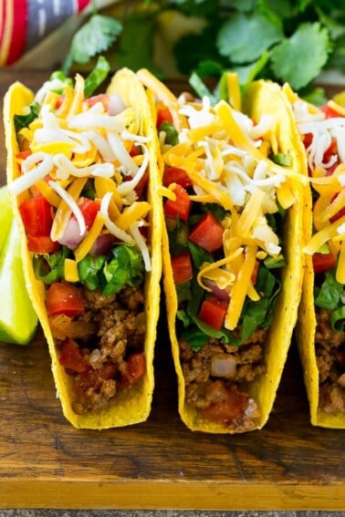 Ground beef tacos in hard taco shells topped with shredded cheese, lettuce, tomato and onion.