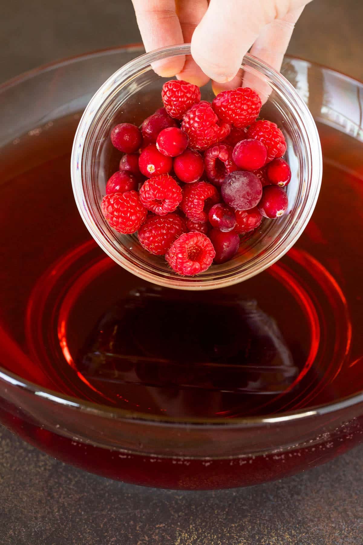 Raspberries and cranberries being poured into a bowl of punch.