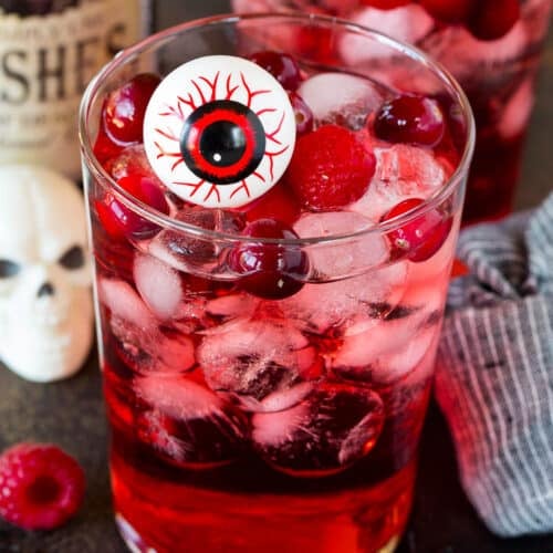 A glass of red Halloween punch with berries and a fake eyeball in it.