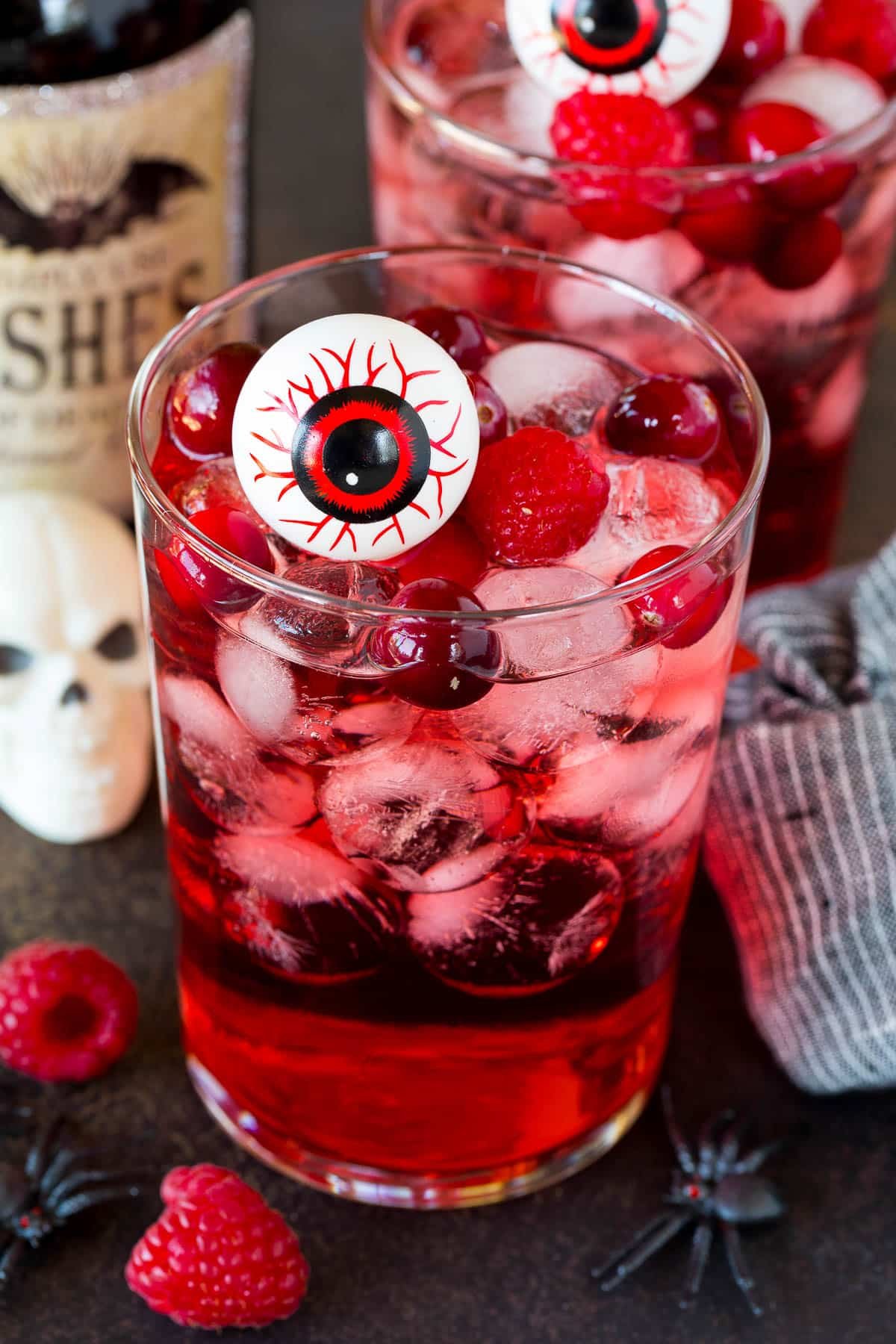 A glass of red Halloween punch with berries and a fake eyeball in it.