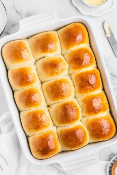 A pan of homemade dinner rolls with butter and a knife on the side.