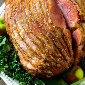 A spiral cut honey baked ham on a serving platter garnished with fresh herbs.