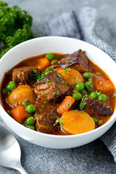 A bowl of Instant Pot beef stew with cubes of meat, potatoes, carrots, onions and peas.