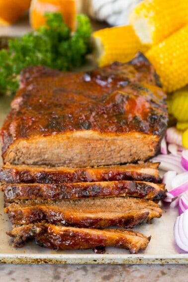 Instant Pot brisket on a tray with red onions and corn on the cob.