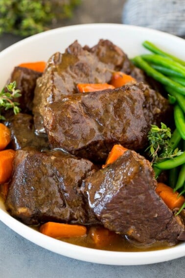 A bowl of Instant Pot short ribs in sauce with carrots and green beans.