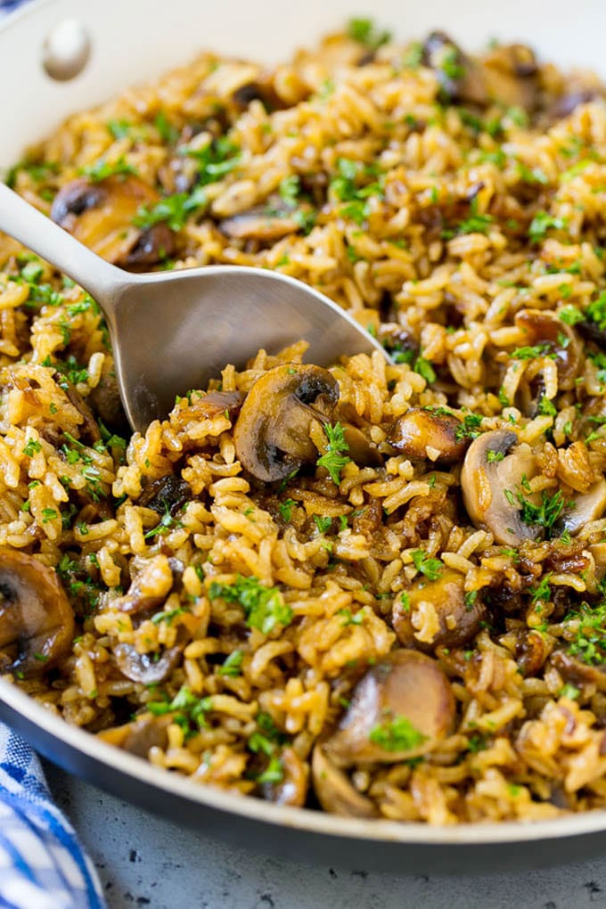 A skillet of easy mushroom rice with a serving spoon in it.