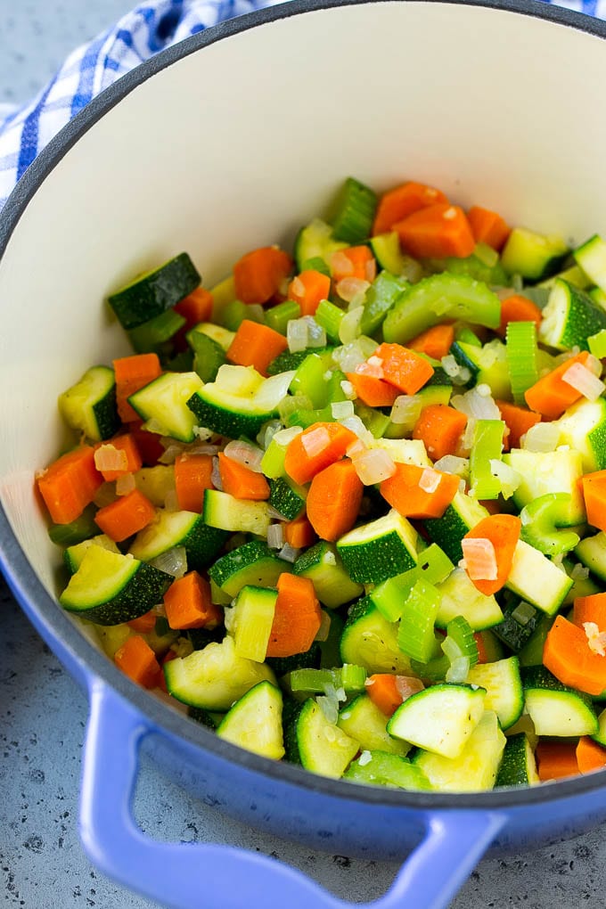 A soup pot full of sauteed onions, celery, carrots and zucchini.