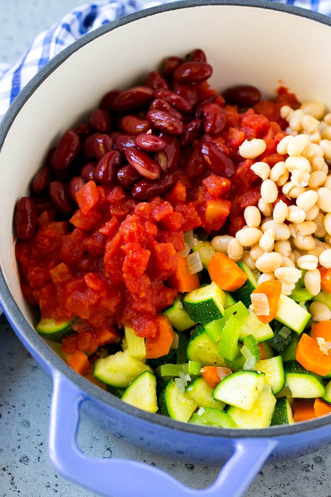 A soup pot full of onions, carrots, zucchini, beans and tomatoes.