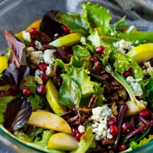 A bowl of pear salad with pomegranate, blue cheese and candied pecans.