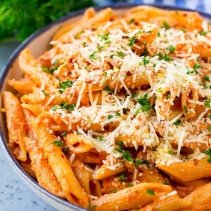 A bowl of penne alla vodka pasta topped with parmesan cheese, parsley and red pepper flakes.