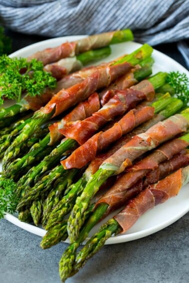 A plate of prosciutto wrapped asparagus garnished with fresh parsley.