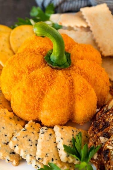 A pumpkin cheese ball on a serving plate surrounded by crackers.