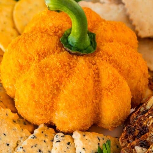 A pumpkin cheese ball on a serving plate surrounded by crackers.