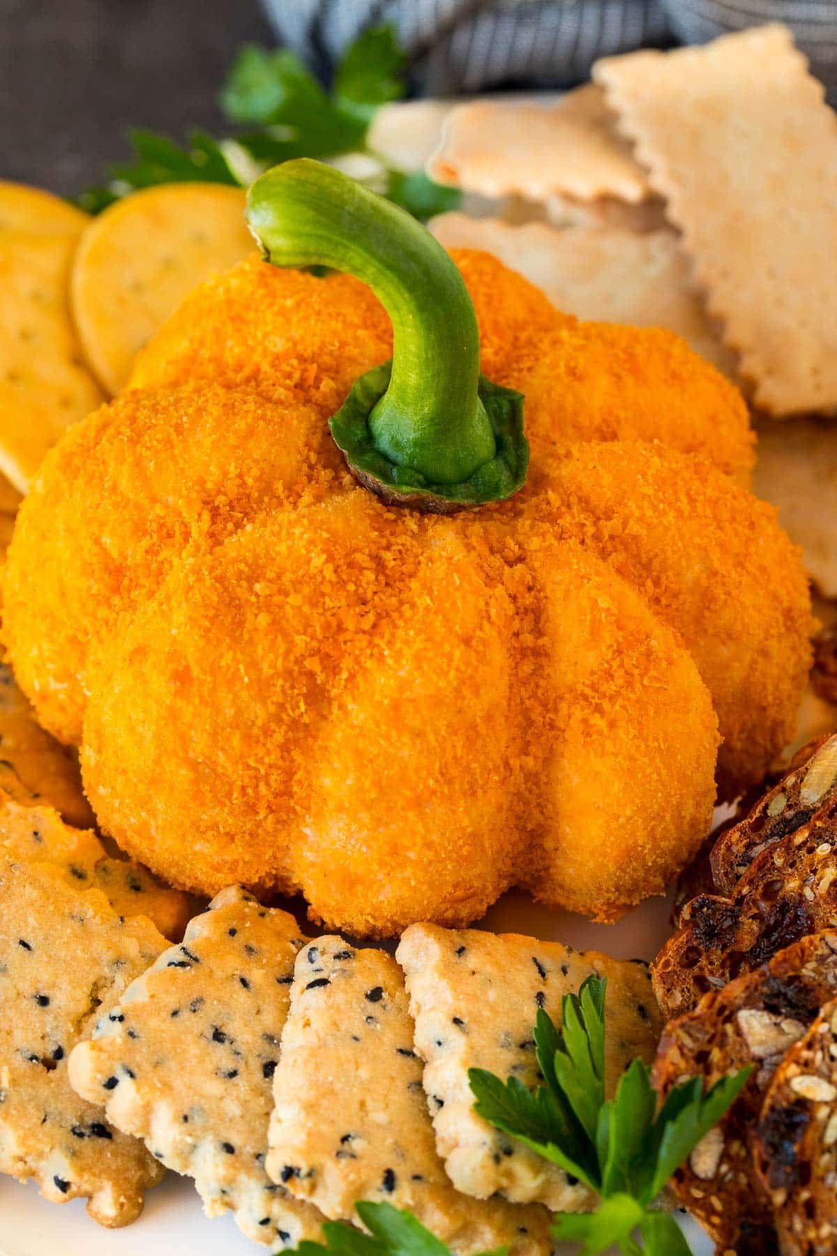 A pumpkin cheese ball on a serving plate surrounded by crackers.