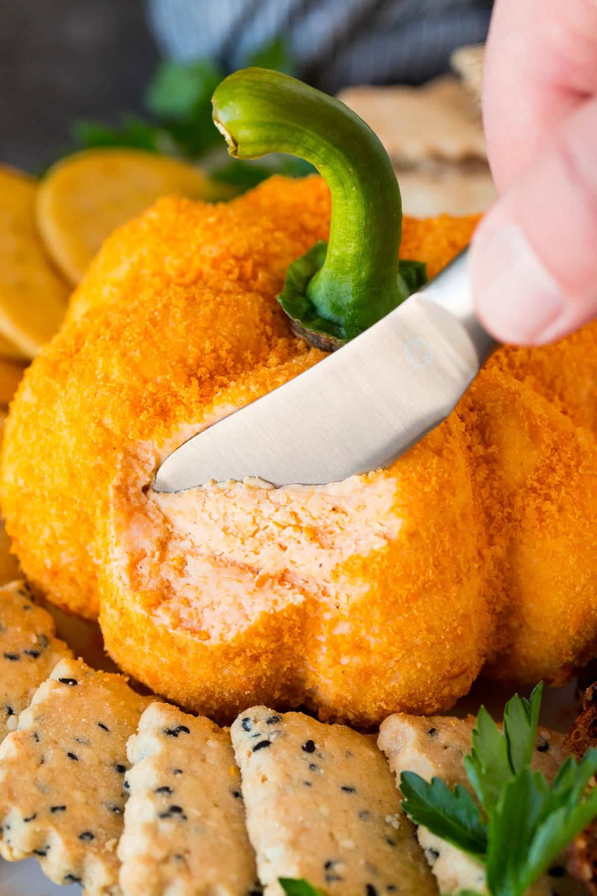 A knife cutting a serving of pumpkin cheese ball.