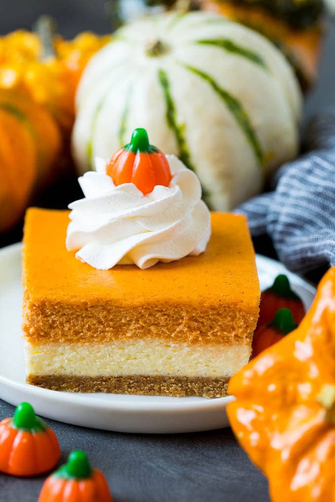 Pumpkin cheesecake bars garnished with whipped cream.