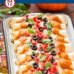 A tray of pumpkin enchiladas topped with sliced olives, diced tomatoes and cilantro.