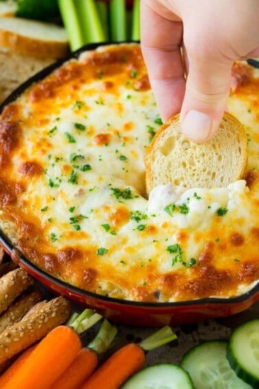 A hand scooping out a serving of Reuben dip with baguette.