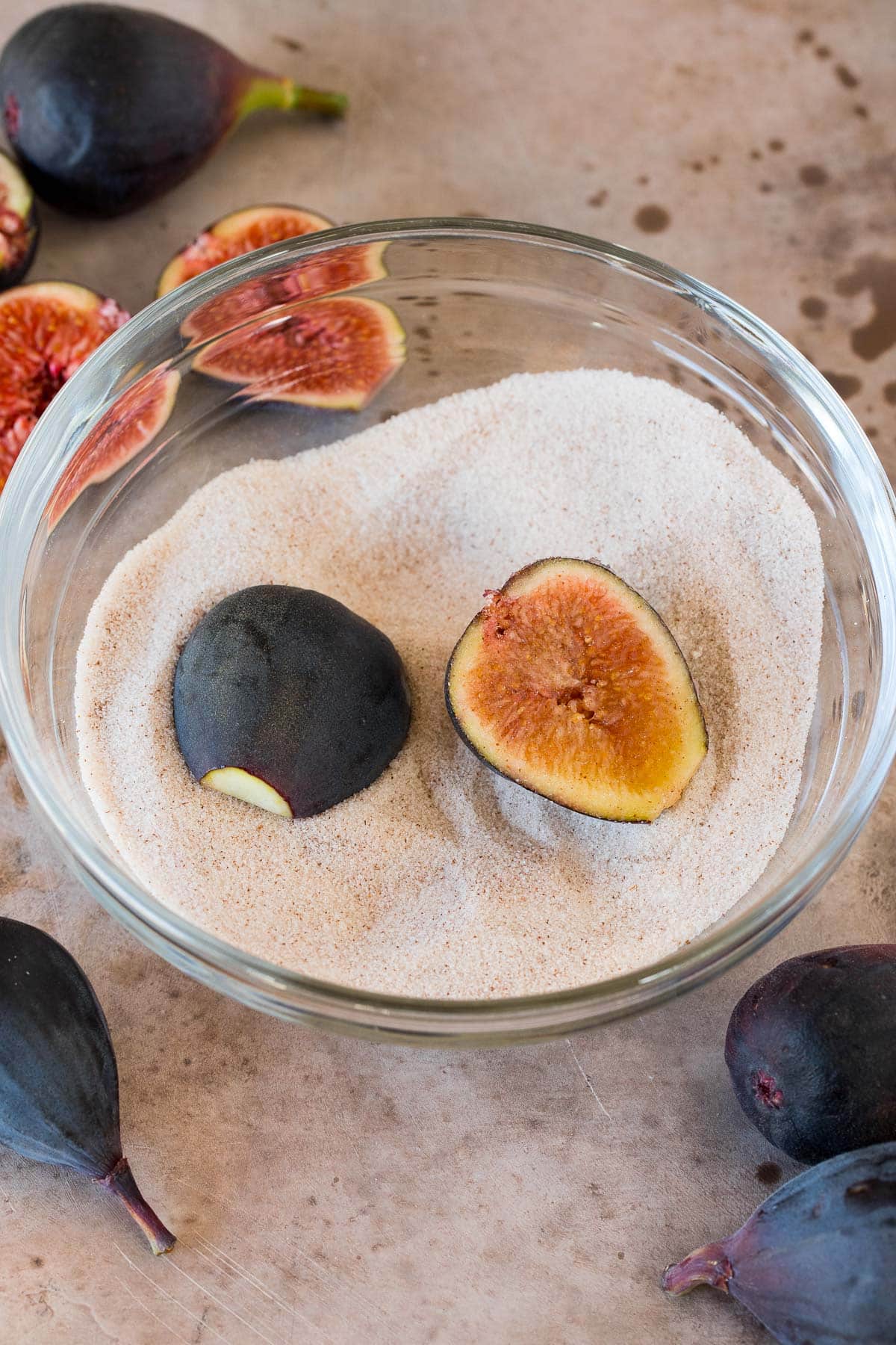 Figs cut in half, in a bowl of cinnamon sugar.