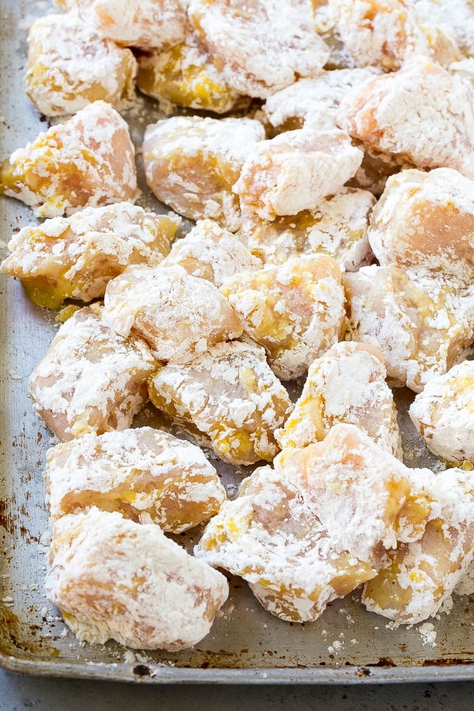 Coated chicken breast pieces on a sheet pan, ready to be fried.