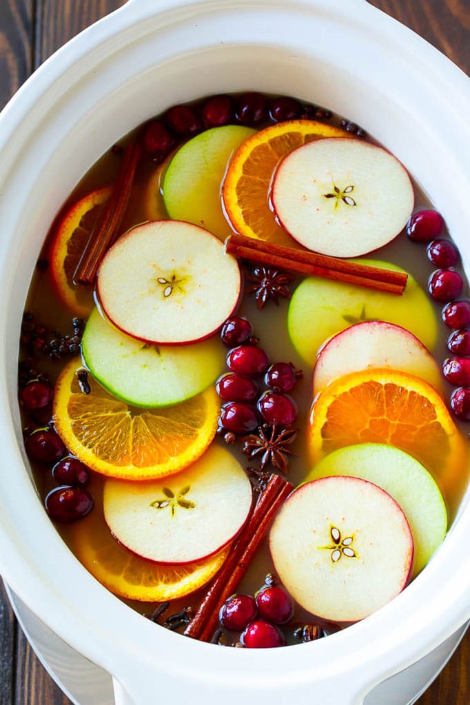 Slow cooker apple cider garnished with apple slices, oranges, cranberries, cinnamon sticks and spices.