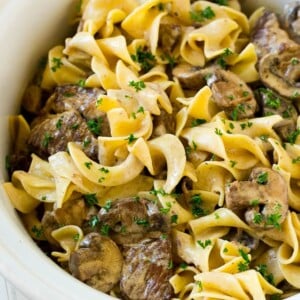 Slow cooker beef stroganoff with chunks of beef, mushrooms and egg noodles topped with parsley.