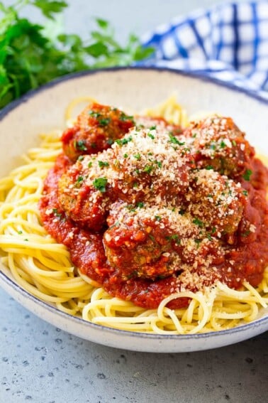 Slow cooker meatballs served over spaghetti, topped with parsley and parmesan cheese.