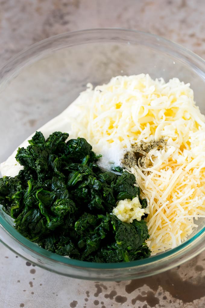 Cooked spinach garlic, shredded cheese, cream cheese and sour cream in a mixing bowl.