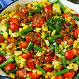 A skillet of succotash topped with bacon and herbs.