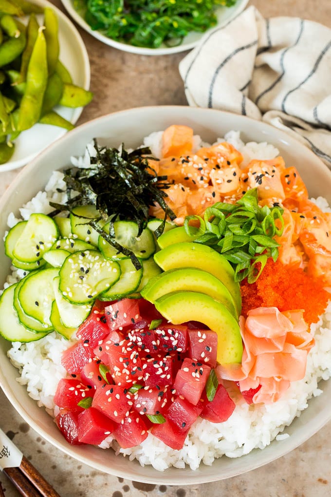 A sushi bowl topped with salmon, ahi, avocado, cucumber and nori.