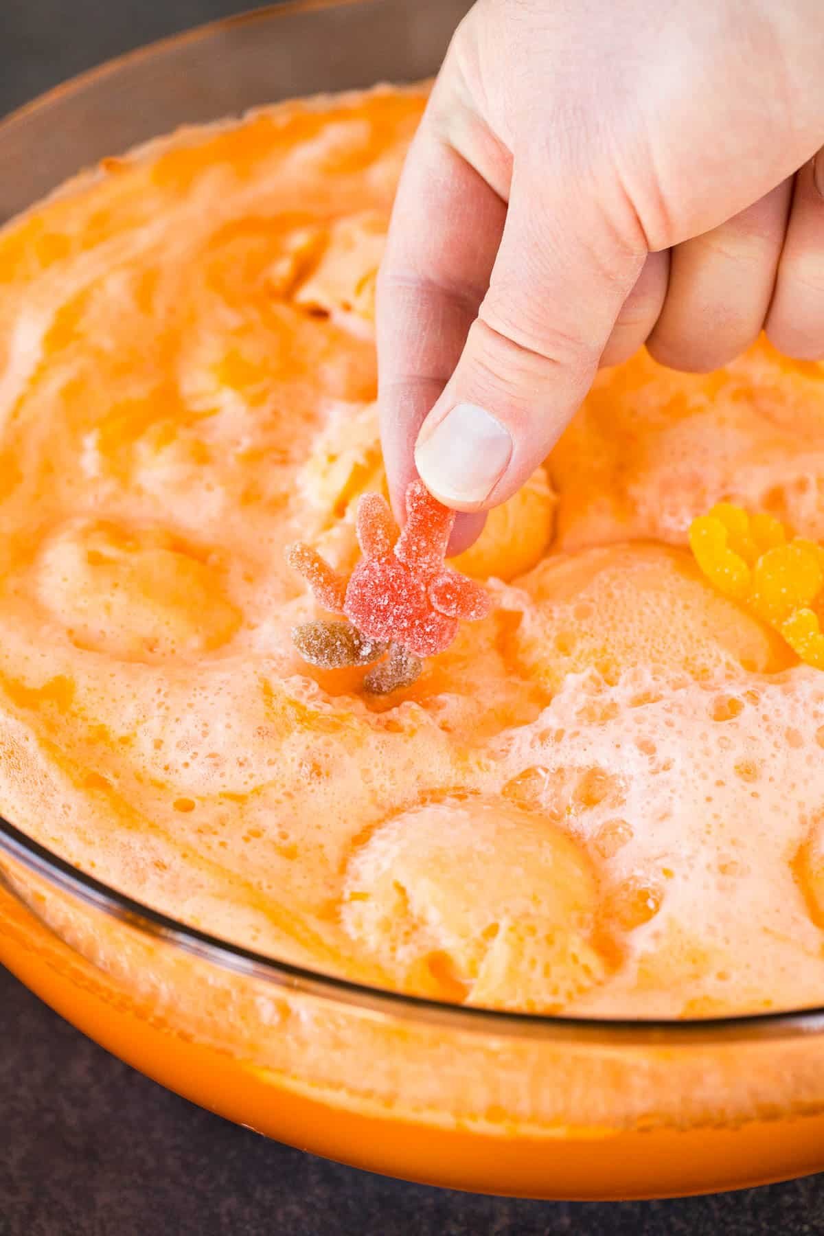 A hand placing a gummy spider into Halloween punch.