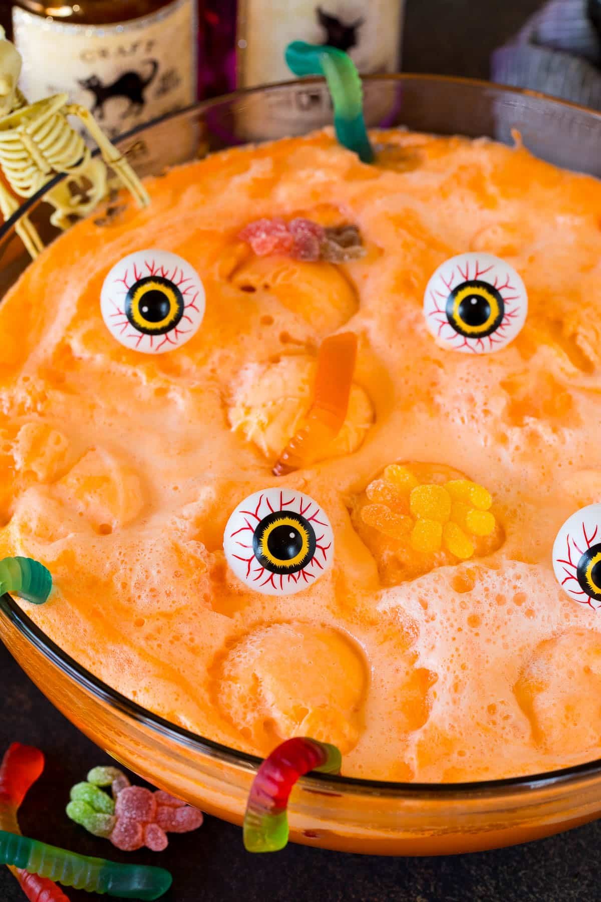 A bowl of witches brew garnished with gummy spiders, gummy worms and plastic eyeballs.