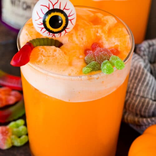 A cup of witches brew topped with a plastic eyeball and gummy candy.