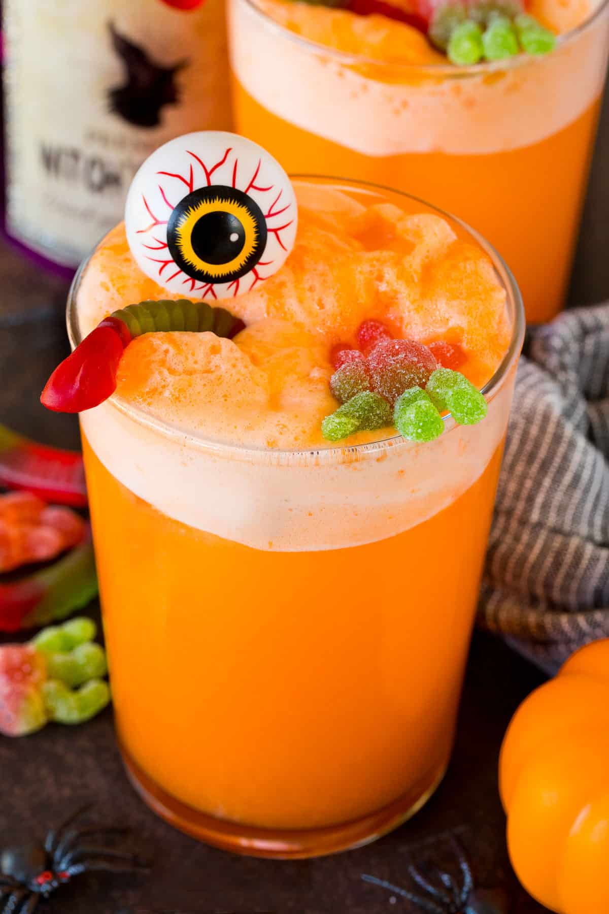 A cup of witches brew topped with a plastic eyeball and gummy candy.